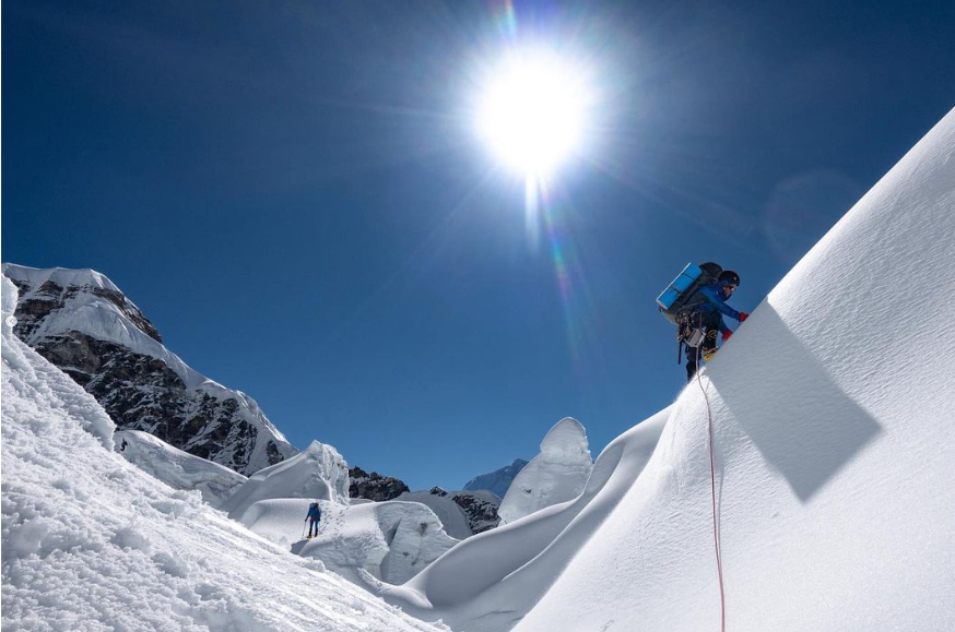 Climber up a snow slope, leaing a serac field behind him