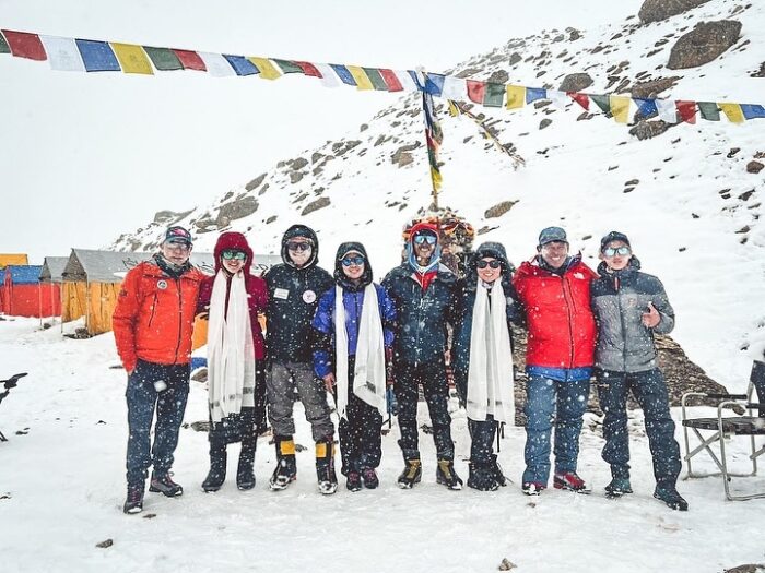 The climbers stand up posing for the photo under a pole with pryer flags in a snowy day