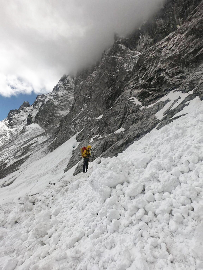 a climber on avalanche debris at the base of a rocky wall