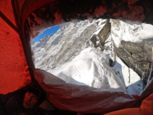 the head of a climber is seen by th open door of a tent, fresh snow behind it, on the East face of Langtang Lirung