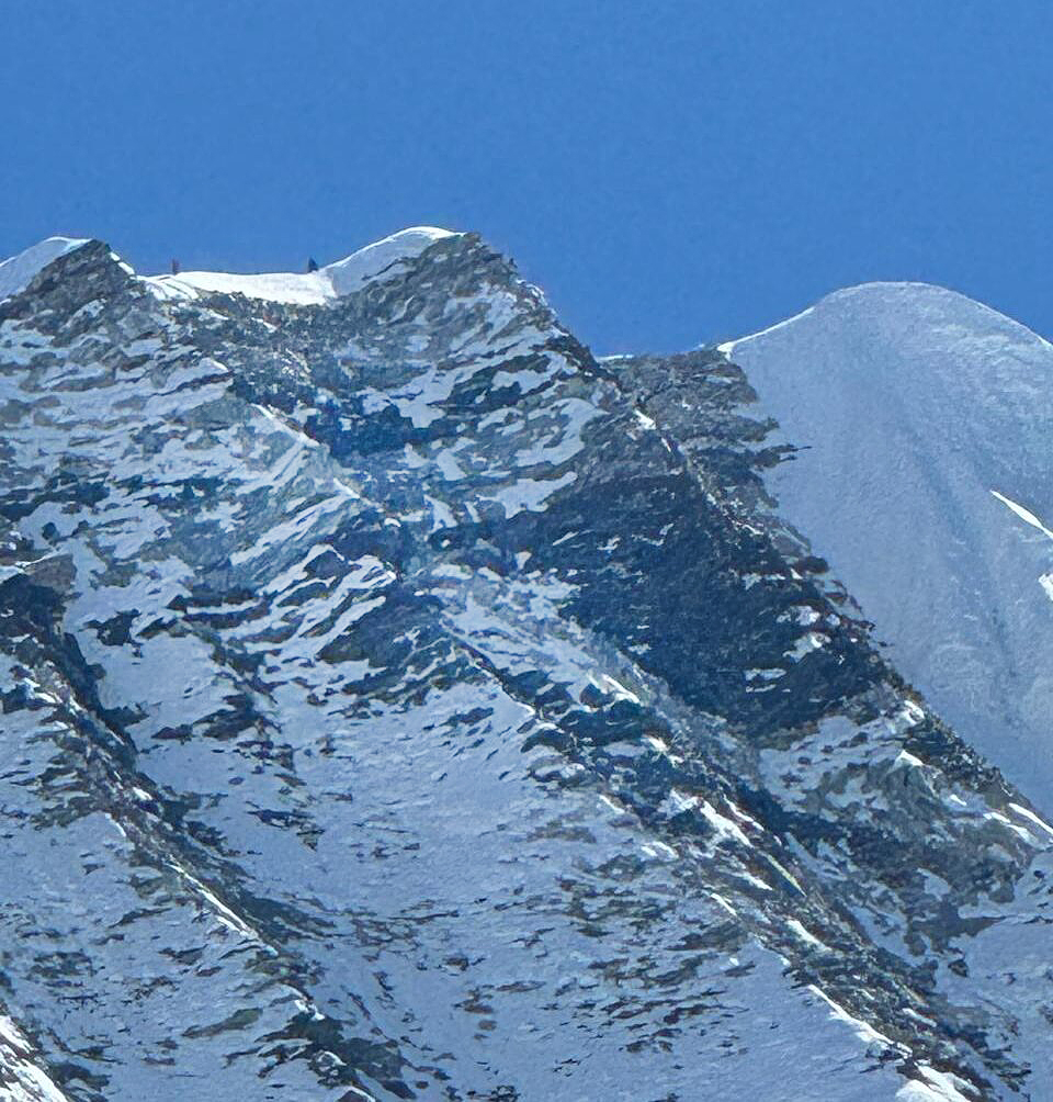 two tiny climbers on top of a ridge, a steep rocky wall below them