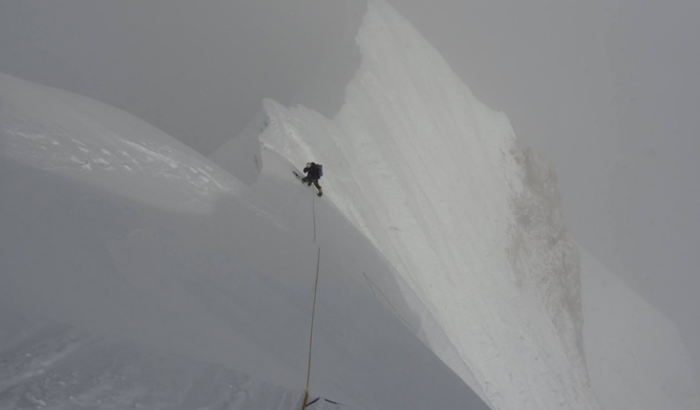 A climber on a sharp, snow ridge in the fog.