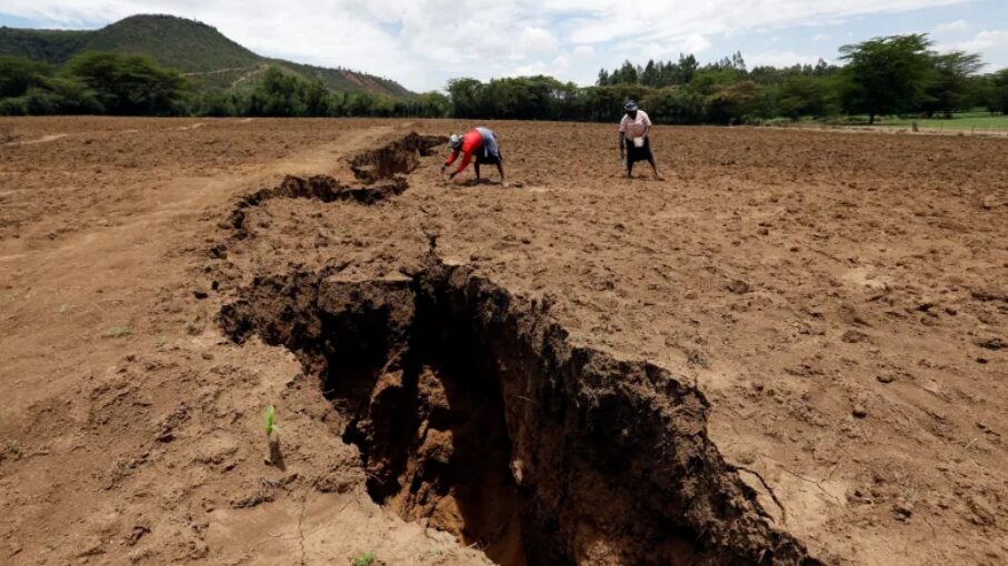 People stand next to a rift in the ground in a dirt field.