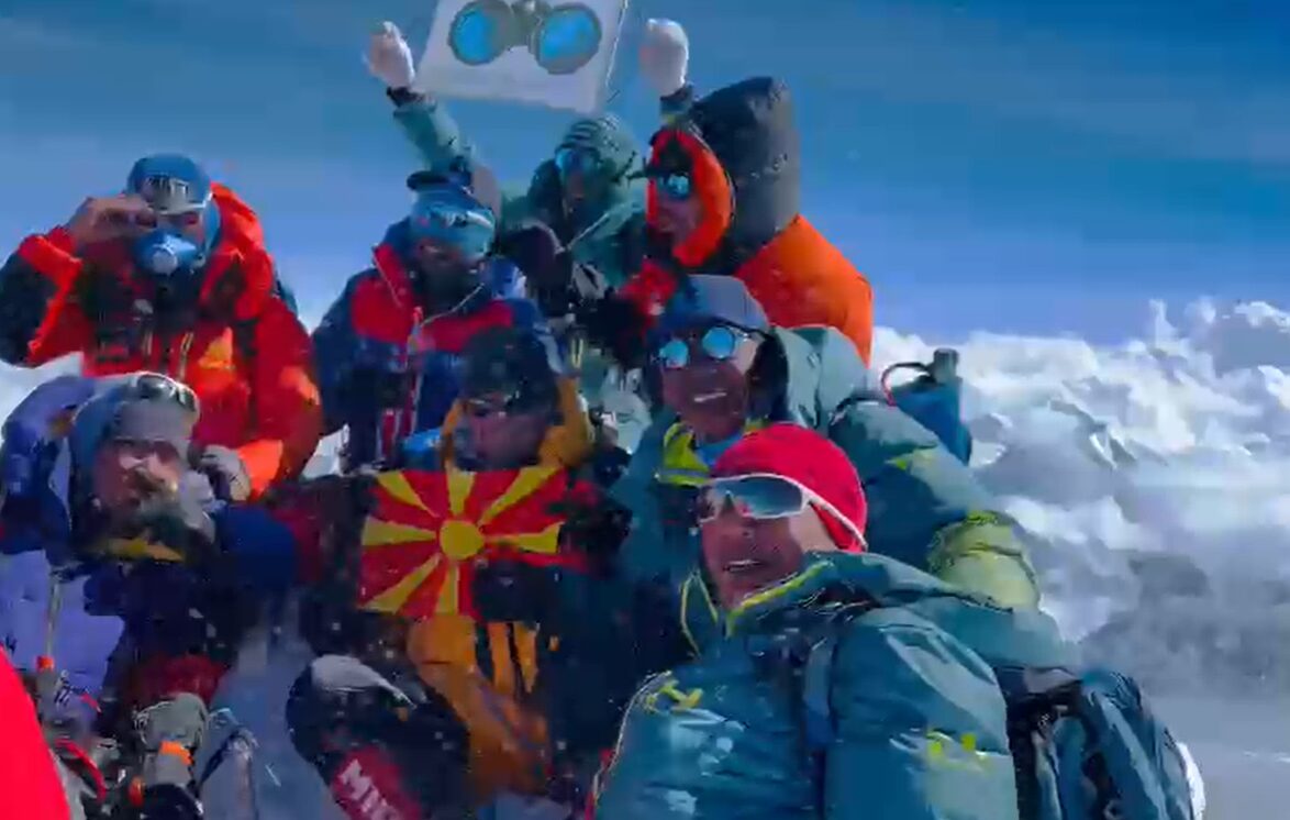 Climbers celebrate and hold flags and banners on the summit os Shisha Pangma