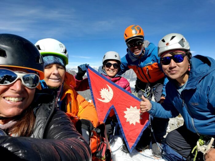 A group of people on a summit holding a Nepali flag. 