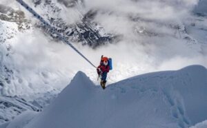 A climber at the end of a rope progressing up a sharp snow ridge.