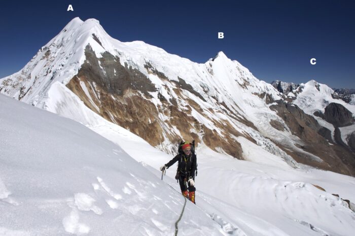 A climbere with three peaks behind him.