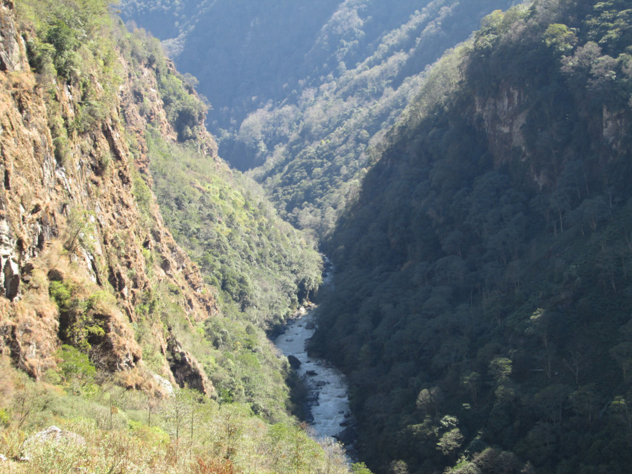 Steep cliffs line with trees surround a thin river.