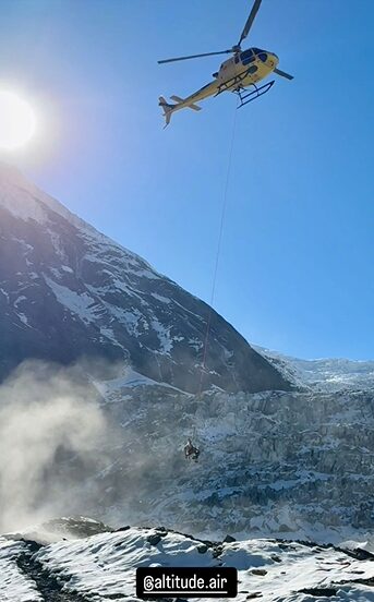 A helicopter approaches base Camp on Dhaulagiri with a body hanging from a long line