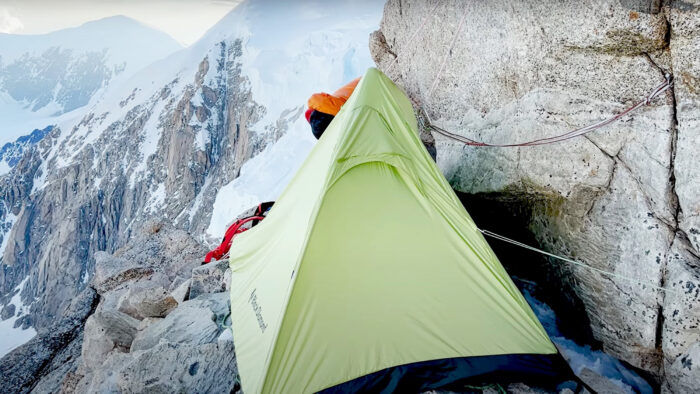 a green tent perched on a rocky ledge