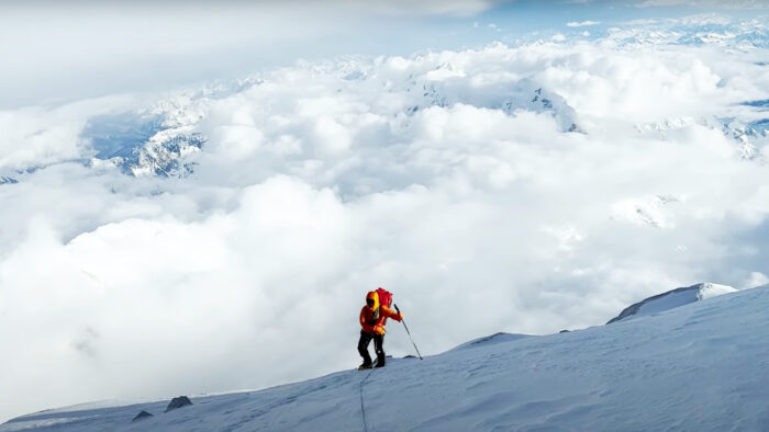 a woman reaches the summit of a mountain with clouds in the background