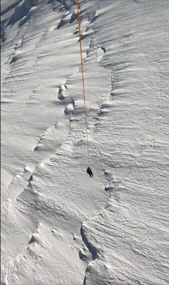 A long cable with a dead body at the end, in front of a snow face