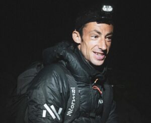 Close shot of Kilian Jornet with a headlamp and primaloft jacket in the night.