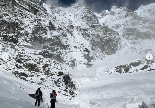 Two climbers under a massive facce of rock and ice.