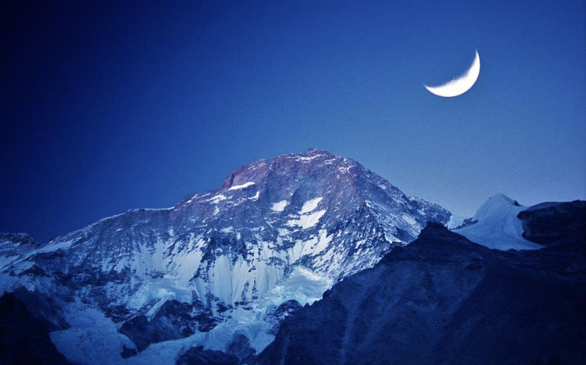 A photo of Makalu at dusk with the crescent moon shining above.