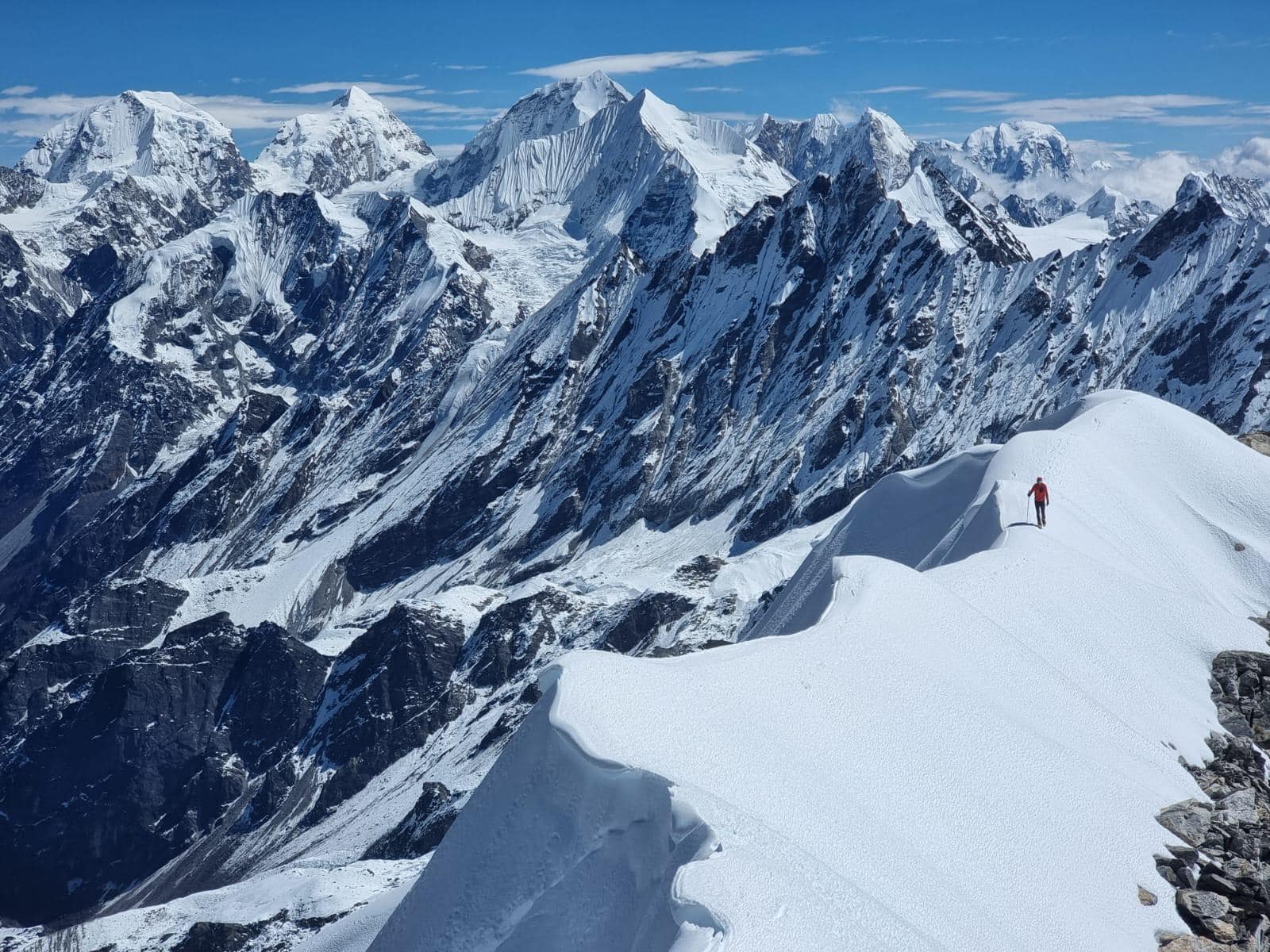 A climber on a snow ridge with a sea of peaks around