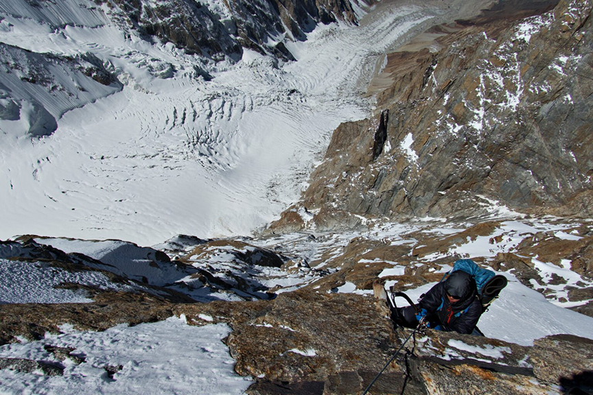 A climber on a vertical rocky section at high altitude.