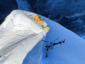 a helicopter on a small snowy shoulder where some tentts are pitched.