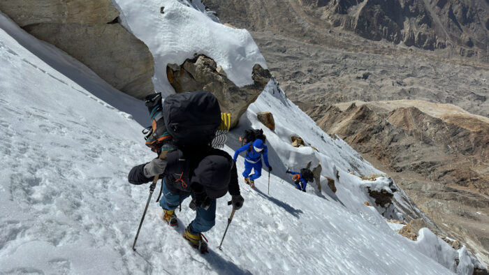 Climbers on crampons up on steep snow ramp.