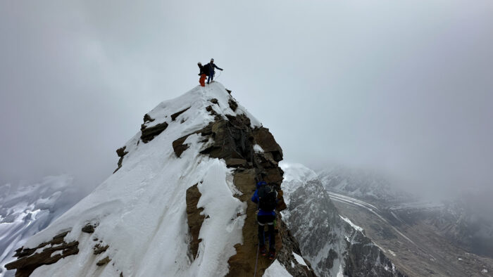 two climbers on a snowy, steep summit in a foggy afternoon.