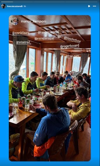 The climbers sitting at a long table in a lodge with windows all around. 