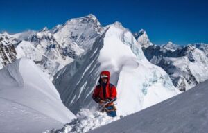 a climber shovels snow on the south side of Cho Oyu, Everest rising in background