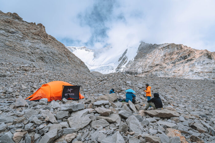 A tent on a dry moraine, snowy peaks in background.