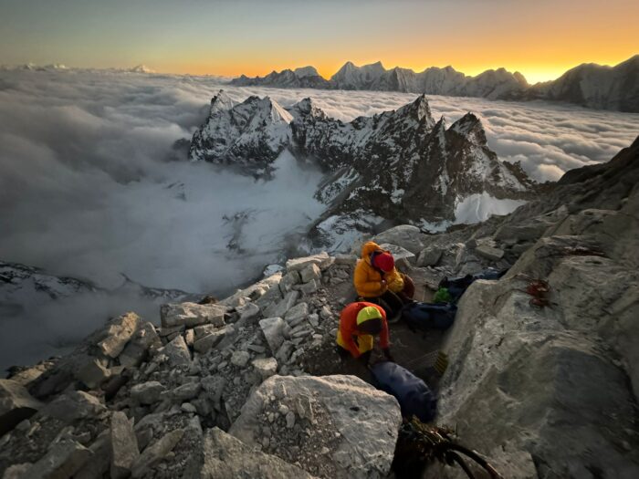 Two climbers prepare for a bivouak on a confortable shelf at sunset