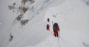 climbers progressing on a snowy ridge with a short section of fixed rope.