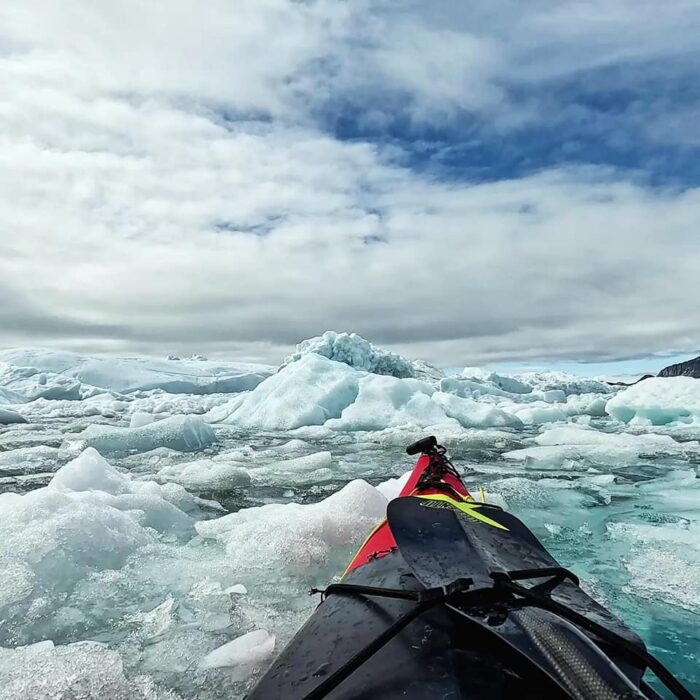 The prow of a kayak in a sea full of ice. 