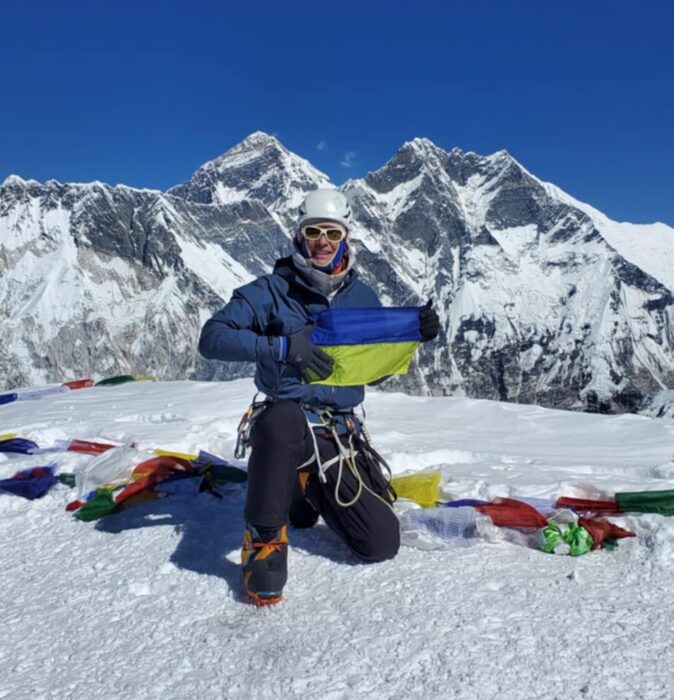 The clibmer kneels and holds an Ukrainian flag on the flat summit of Ama Dablam