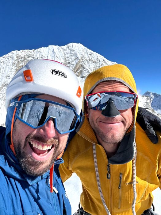 Climbers selfie with mirror-glasses , a summit behind them. 