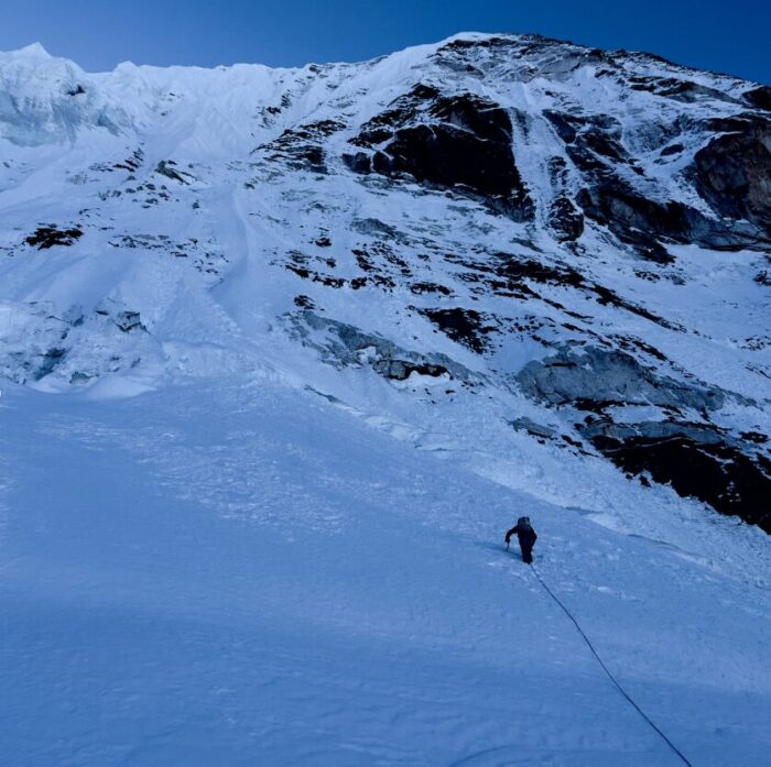 A climber with a rope behind him geading toward an ice face. 