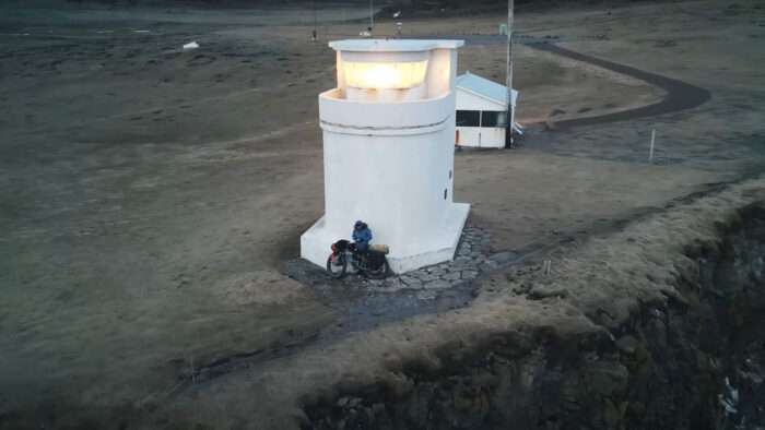 an aerial shot of a man and bike leaning against a lighthouse 