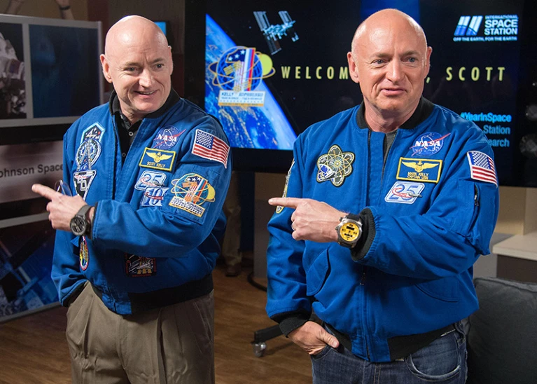 Two nearly identical men stand in NASA attire, pointing to the left.