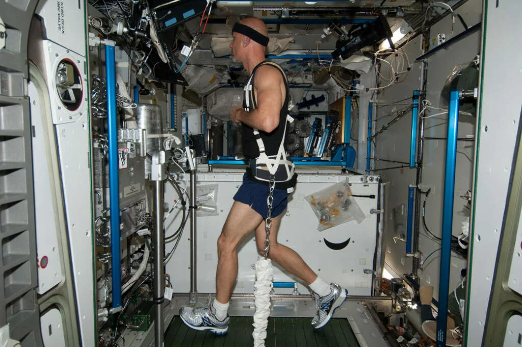 A man attached to a harness pulling him down runs on a treadmill.