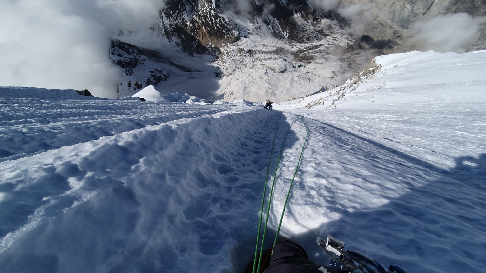 A tiny climber at the end of a rope, on very steep ice terrain.