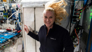 a woman in space floats next to a handwritten sign that says "ISS voting booth"