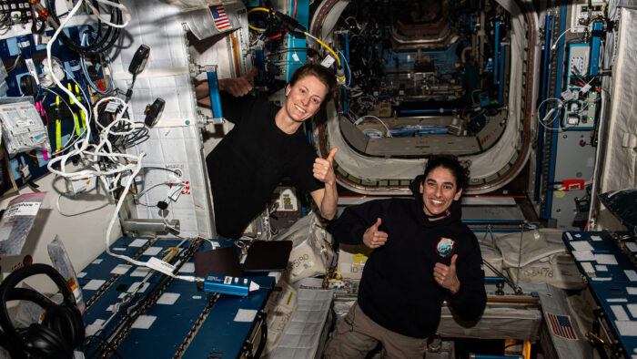 two women floating in space give a thumbs up