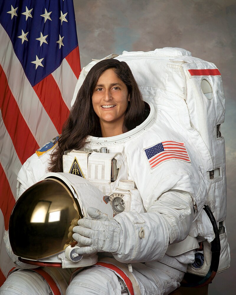 A woman in a space suit holds her helmet.