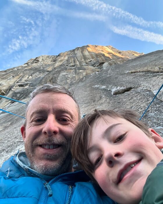 Tommy Caldwell and his son look at the camera, with the face of El Capitan rising above them. 