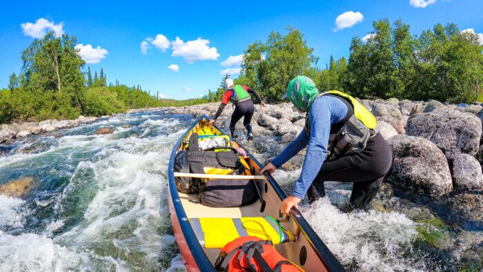 Two men haul a canoe over rocks. 