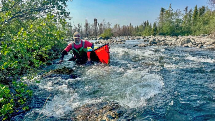 a man drags a canoe over rocks