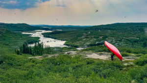 a man holds a canoe while looking out over a river