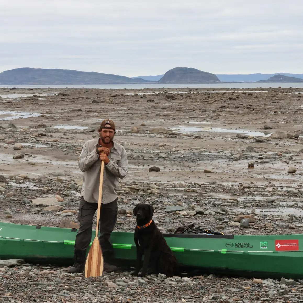 man standing with dog and canoe on mud flats