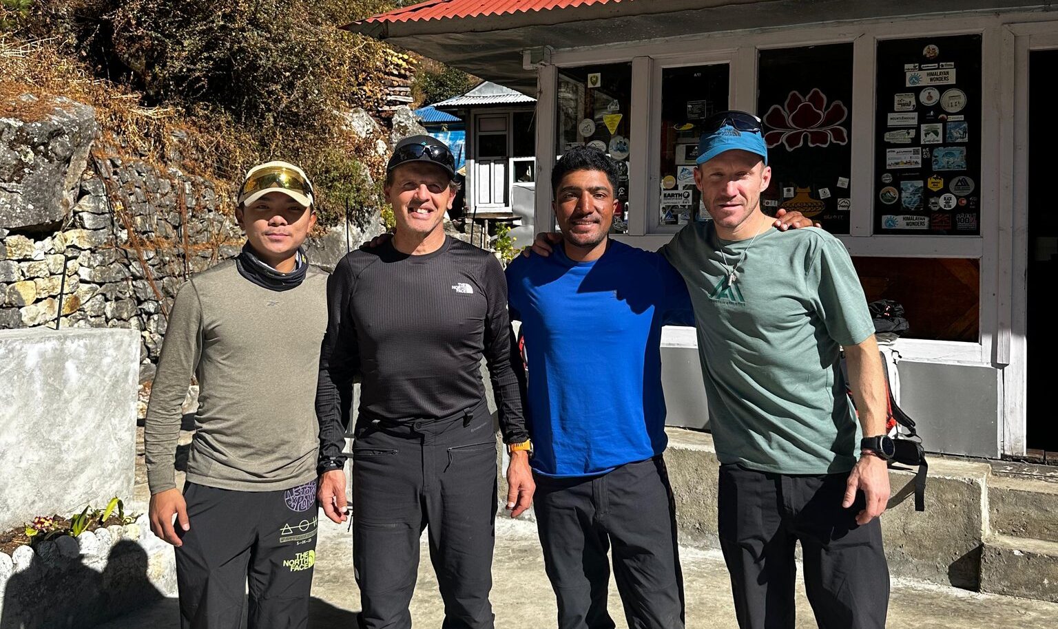 The climbers pose with light shirts in a sunny day by a lodge.