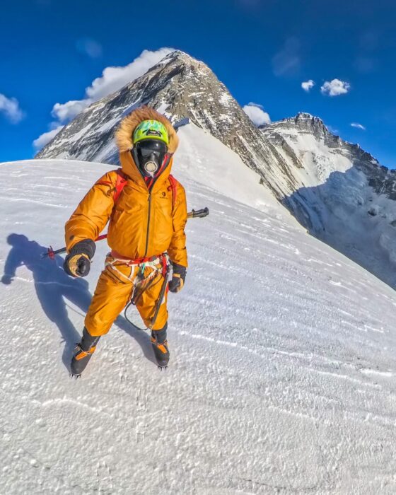 Kobusch on a snowy ridge, the pyramidal summit of Everest behind him.