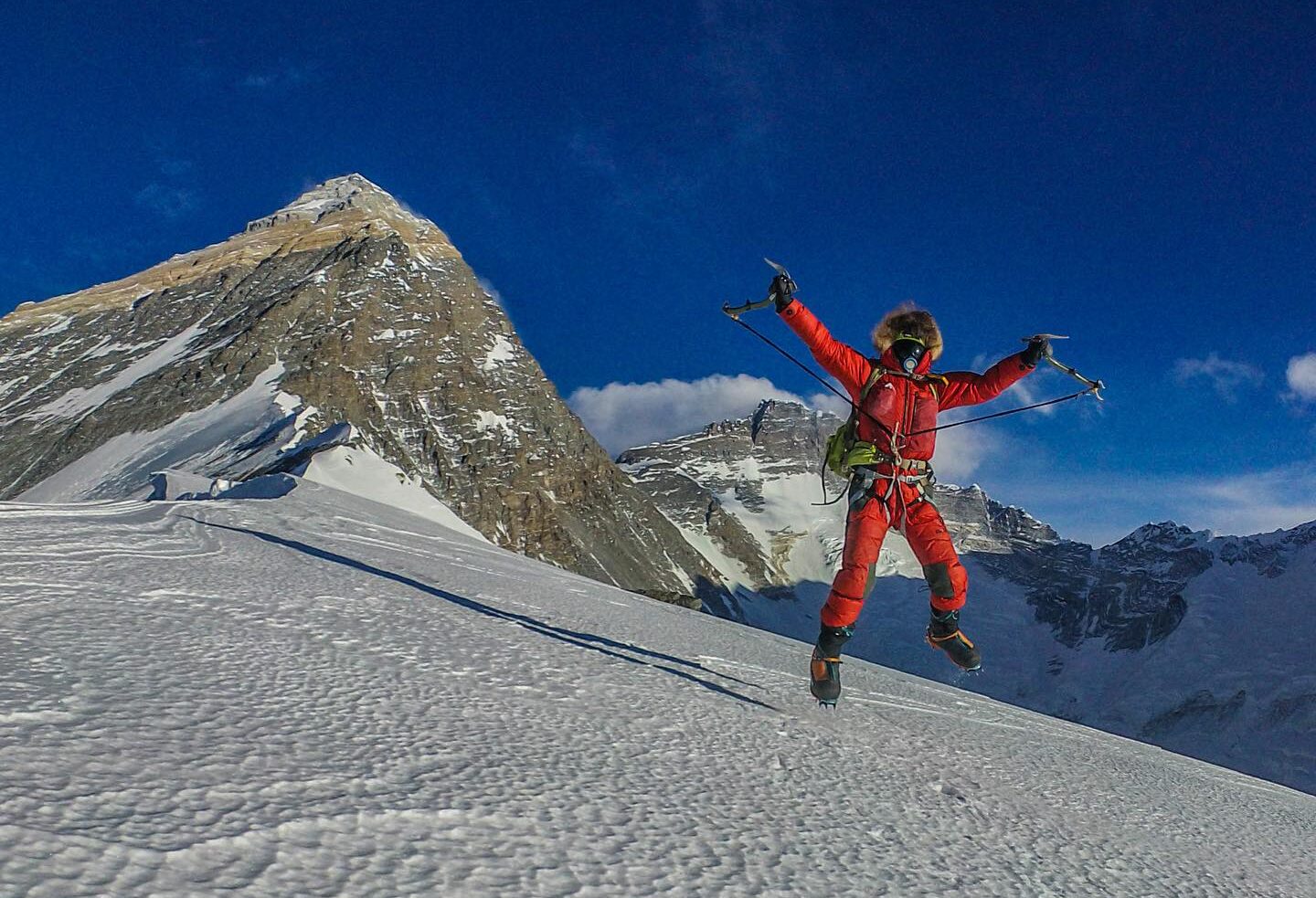 Kobusch jumps on the hard snow of the ridge, Everest summit behind.