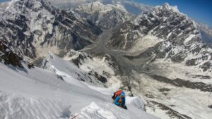 A climber on a steep snow slope, the glacial valley at his feet