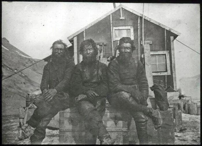 three men in front of a hut